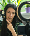 Gredzena formas lampa ar USB kabeli un telefonu turetaju, fonā cilvēks filmē video