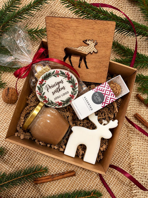 Ziemassvētku dāvana Ziemas miers ar personalizējamu koka paliktni ar aļņa motīvu, piparkūku ar uzņēmuma logo, medu ar kanēli, sveci un PŪRE konfektēm
